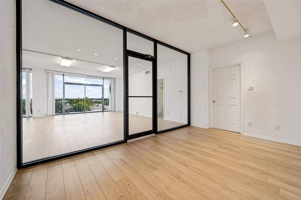 5200 Keller Springs Road, #522, Dallas, TX 75248 Floor-to-ceiling glass partition with black metal framing, wood-finish flooring, adjustable track lighting, and expansive glass sliding doors
