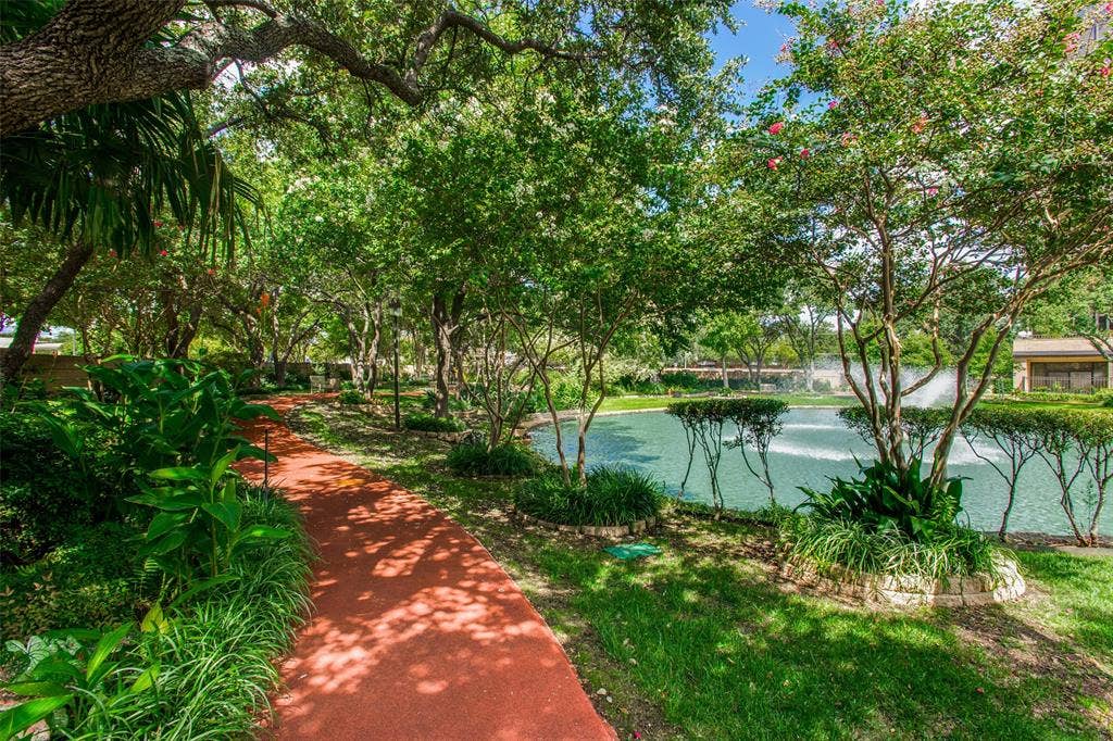 5200 Keller Springs Road, #522, Dallas, TX 75248 Landscaped grounds featuring a winding paved path, mature shade trees, stone-edged garden beds, and a decorative pond with a water feature