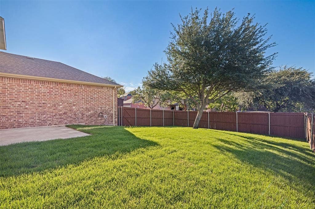 1380 Riverside Oaks Drive, Rockwall, TX 75087 Backyard featuring a brick exterior wall, a concrete patio, a mature tree, and a solid wood-tone privacy fence