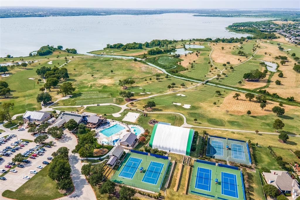 1380 Riverside Oaks Drive, Rockwall, TX 75087 Aerial perspective of a multi-purpose recreational complex featuring multiple tennis courts, a swimming pool, a covered sports structure, and expansive green space bordering a large lake