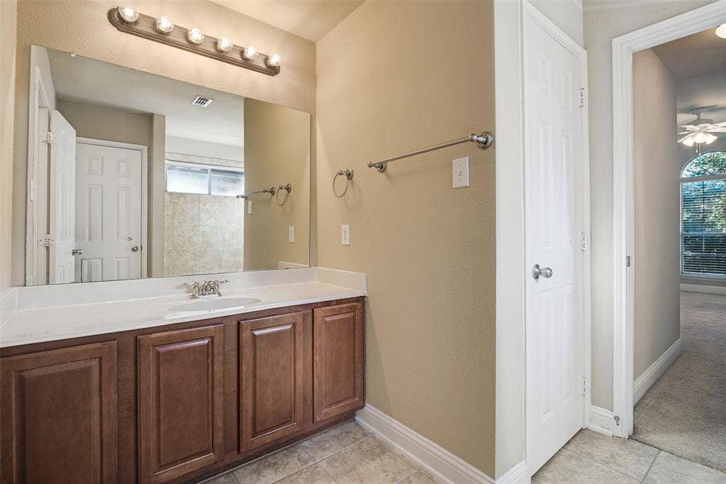 1380 Riverside Oaks Drive, Rockwall, TX 75087 Bathroom vanity featuring wood cabinetry, solid-surface countertop with an integrated sink, full-width wall mirror, and multi-bulb vanity light fixture
