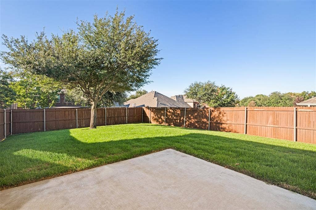 1380 Riverside Oaks Drive, Rockwall, TX 75087 Backyard featuring a concrete patio, wood privacy fencing, and a mature tree