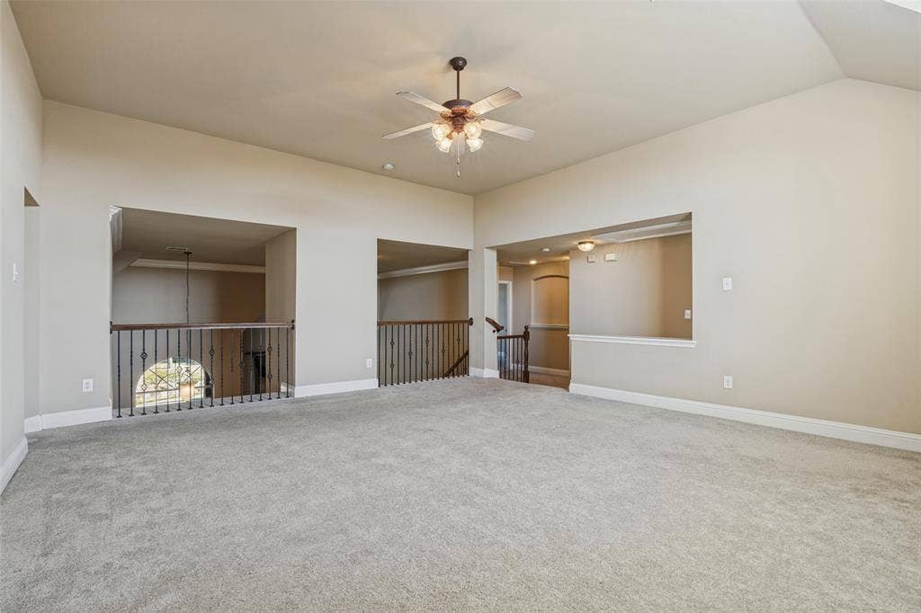 1380 Riverside Oaks Drive, Rockwall, TX 75087 Vaulted ceiling featuring a central ceiling fan with multi-light fixture, carpeted flooring, and decorative metal baluster railings