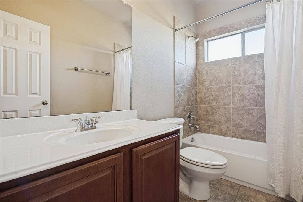 1380 Riverside Oaks Drive, Rockwall, TX 75087 Bathroom featuring a dark wood-finish vanity with a white countertop, inset sink, polished metal faucet, full-width wall mirror, and a tub-shower combination with tile surround