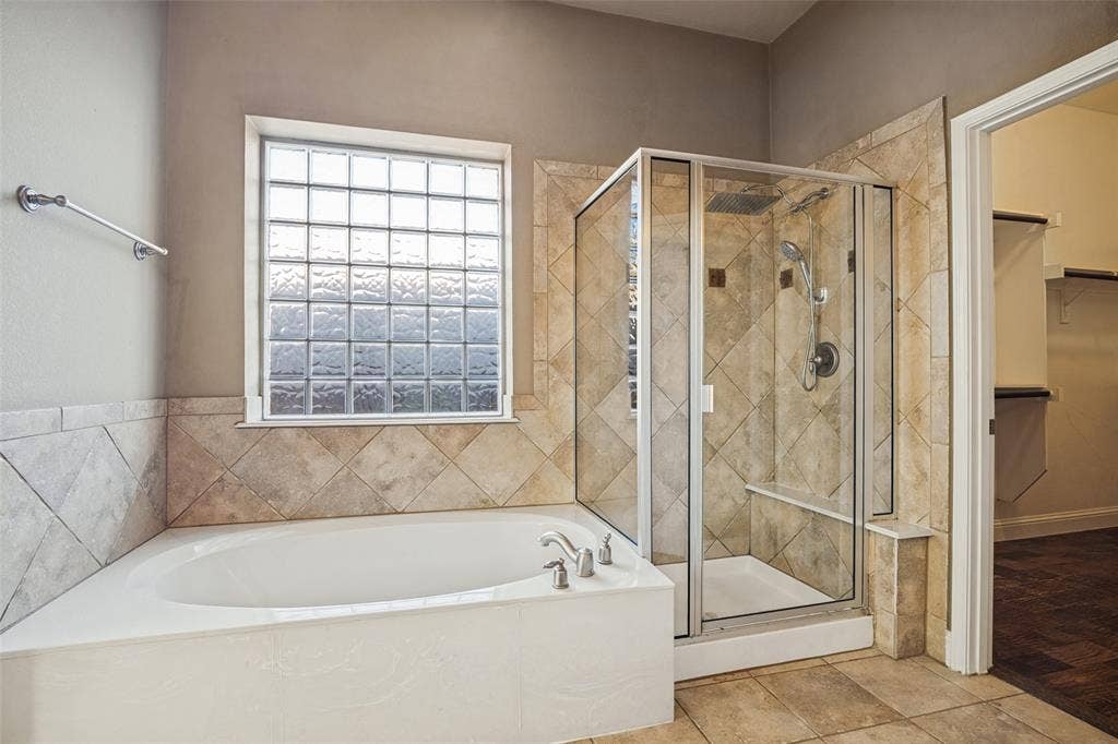 1380 Riverside Oaks Drive, Rockwall, TX 75087 Bathroom featuring a drop-in soaking tub, a glass-enclosed shower with a rainfall showerhead, diamond-patterned wall tile, and a glass block window