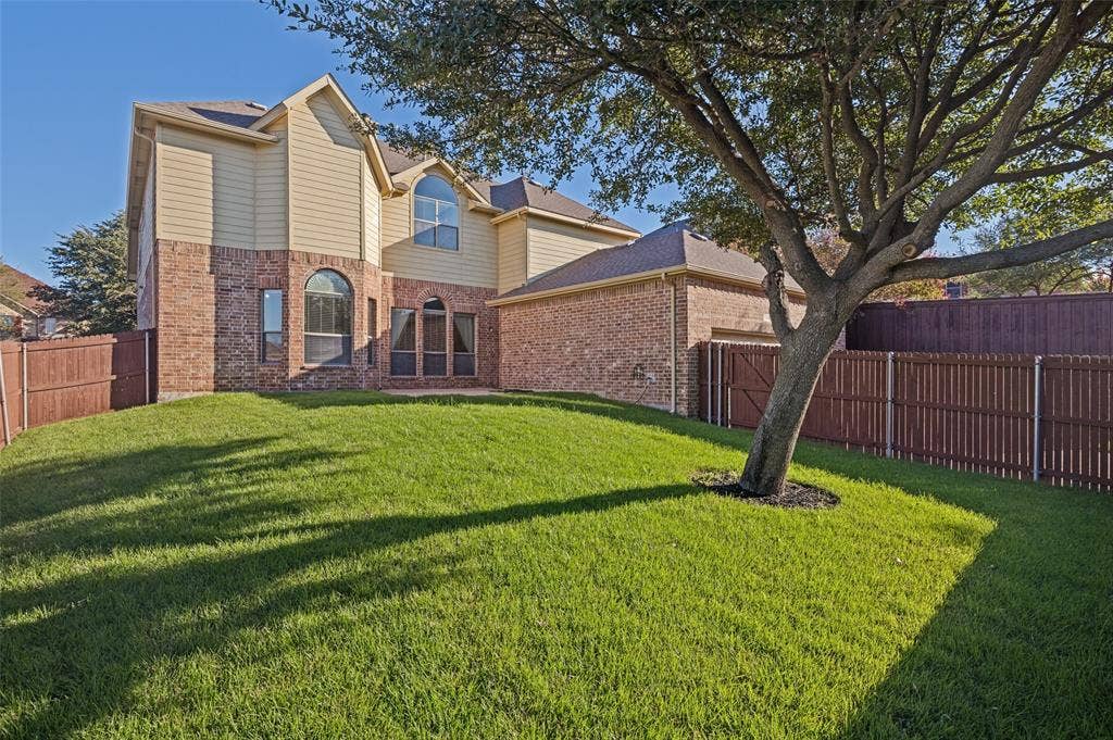 1380 Riverside Oaks Drive, Rockwall, TX 75087 Rear exterior featuring a brick and siding facade, arched windows, and a fenced backyard with a mature tree