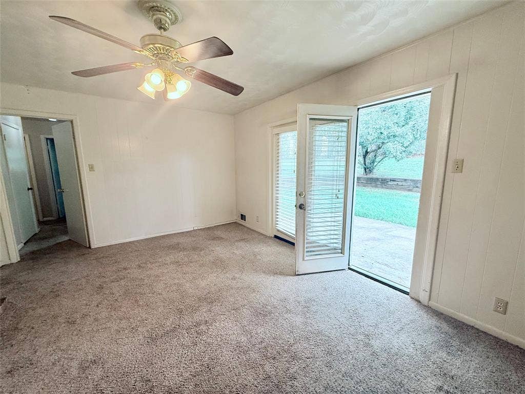 1500 S Houston, Denison, TX 75020 Interior space featuring carpeting, a ceiling fan with integrated lighting, paneled walls, and a glass-paneled door providing access to a concrete patio