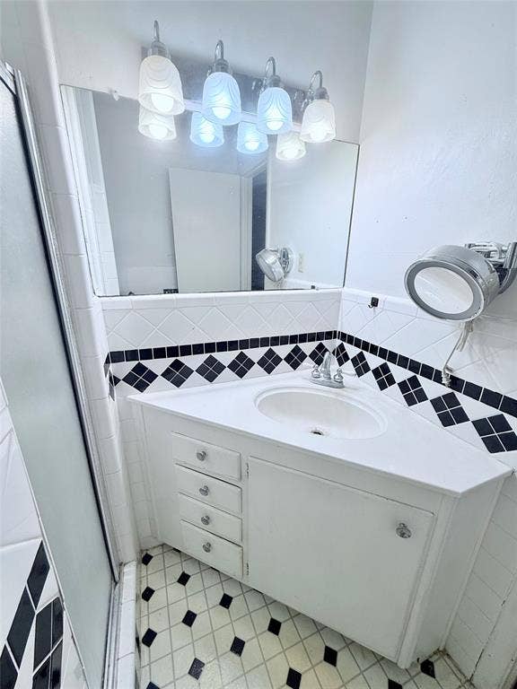 1500 S Houston, Denison, TX 75020 Corner vanity featuring white cabinetry, a molded sink, diamond-pattern tile backsplash, and a multi-light fixture with glass shades