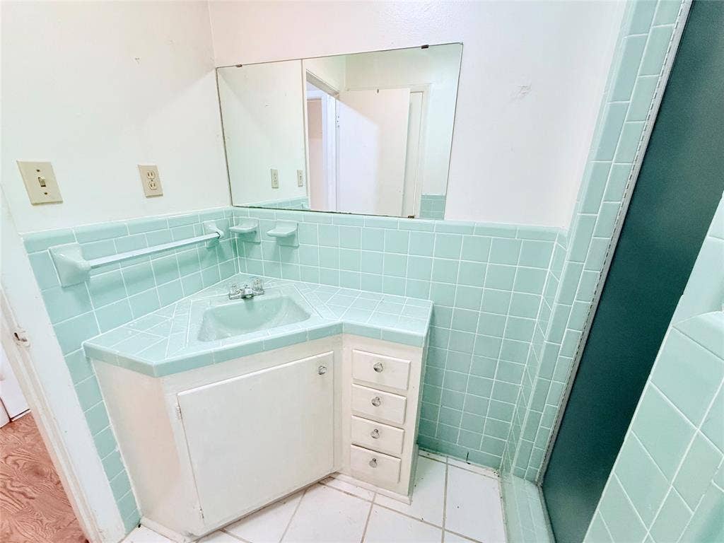 1500 S Houston, Denison, TX 75020 Corner vanity featuring a recessed basin, integrated tile countertop, and white cabinetry, accented by light green square wall tiling, a built-in towel rack, and a large wall-mounted mirror