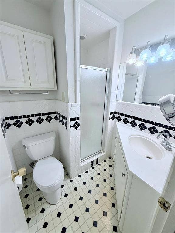 1500 S Houston, Denison, TX 75020 Bathroom featuring a corner vanity with integrated sink, shower enclosure with frosted glass door, wall-mounted cabinetry, geometric tile flooring, and decorative diamond-pattern wall tile accents