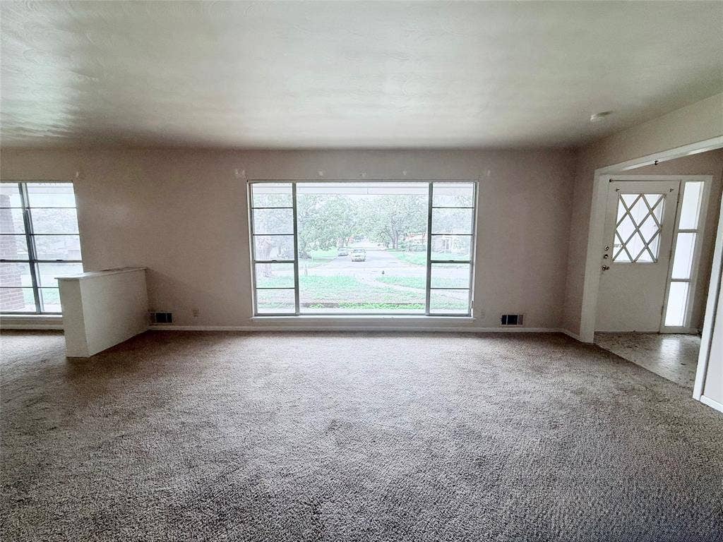 1500 S Houston, Denison, TX 75020 Spacious room featuring a large picture window, wall-to-wall carpeting, and an entry door with diamond-patterned glass inlay