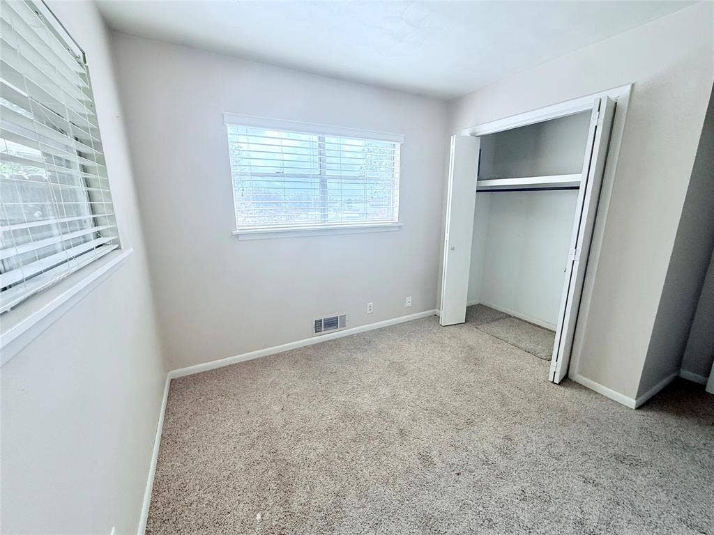 1500 S Houston, Denison, TX 75020 Neutral-toned room featuring neutral carpeting, white walls, horizontal window blinds, and a built-in closet with folding doors
