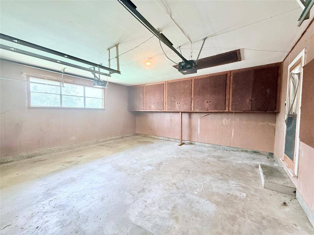 1500 S Houston, Denison, TX 75020 Multi-car garage featuring concrete flooring, built-in wooden cabinetry, a multi-pane window, and an integrated garage door opener system