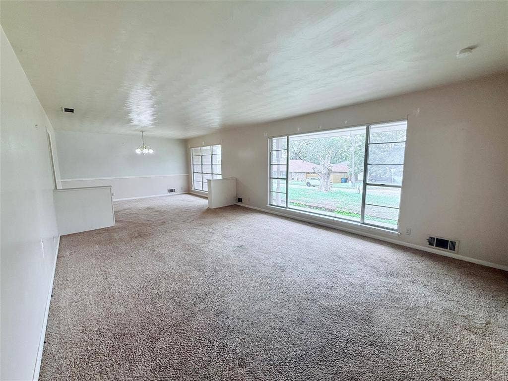 1500 S Houston, Denison, TX 75020 Spacious interior featuring neutral carpeting, a large picture window, multi-pane accent windows, chair rail molding, and a tiered architectural half-wall