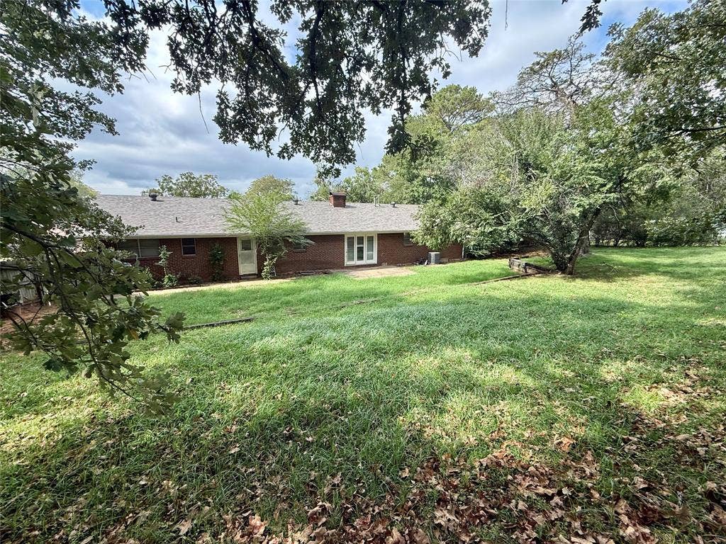 1500 S Houston, Denison, TX 75020 Exterior elevation featuring a red brick facade, asphalt shingle roof, expansive backyard, and mature trees