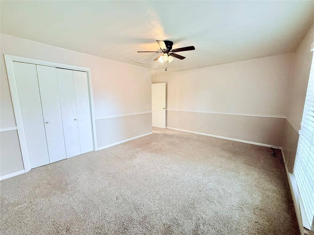 1500 S Houston, Denison, TX 75020 Interior space featuring carpeted flooring, two-paneled closet doors, a central ceiling fan with integrated lighting, and chair rail molding