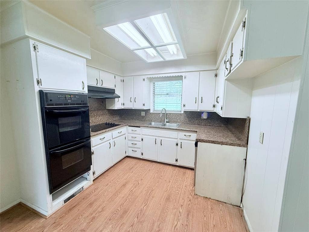 1500 S Houston, Denison, TX 75020 Kitchen featuring white cabinetry, wood-finish flooring, a built-in double oven, stone-patterned countertops, and a recessed skylight