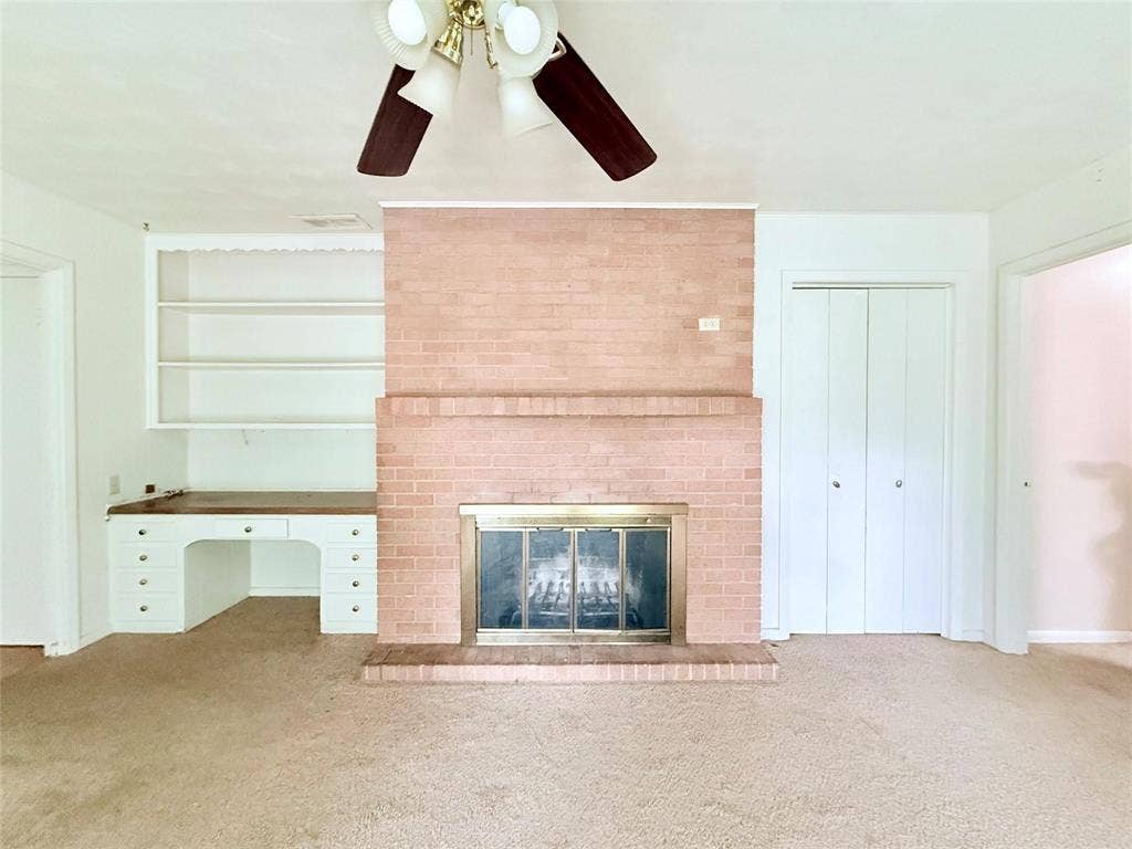 1500 S Houston, Denison, TX 75020 Brick fireplace with a metal screen and hearth, built-in desk with drawers, open wall shelving, and a ceiling-mounted light fixture
