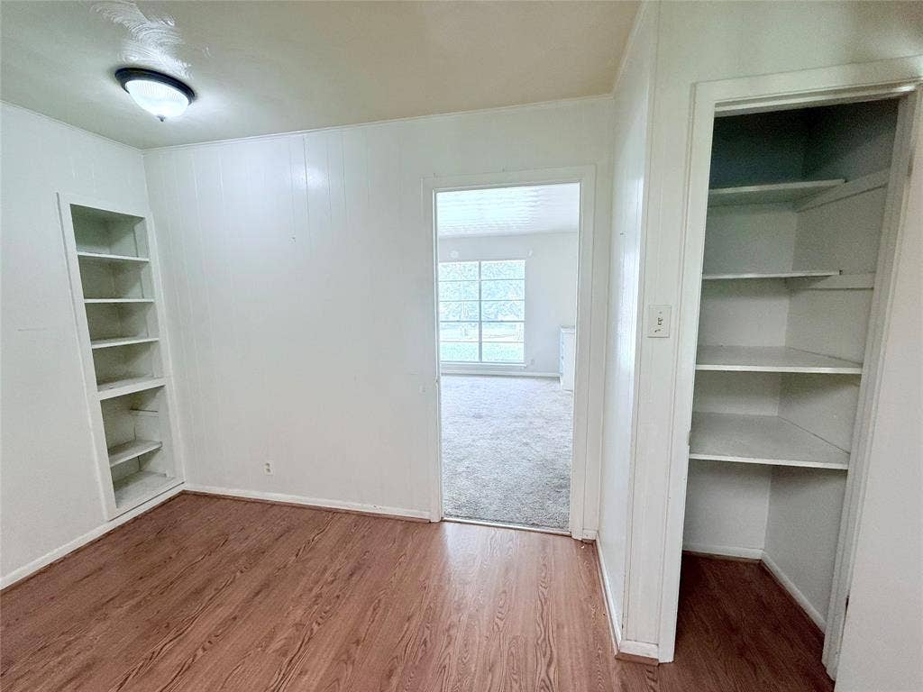 1500 S Houston, Denison, TX 75020 Room interior featuring wood-finish flooring, built-in wall shelving, a flush-mount light fixture, and an open closet with built-in storage shelves