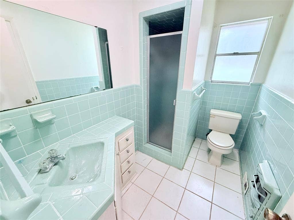 1500 S Houston, Denison, TX 75020 Bathroom featuring square ceramic wall tiling, a vanity with a tiled countertop and integrated sink, a walk-in shower enclosure with a frosted door, and white floor tile
