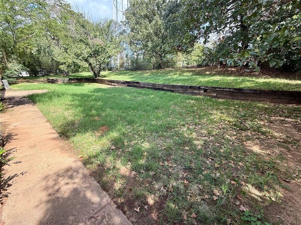 1500 S Houston, Denison, TX 75020 Rear yard featuring a concrete path, tiered landscape retaining walls, grass lawn, and mature trees