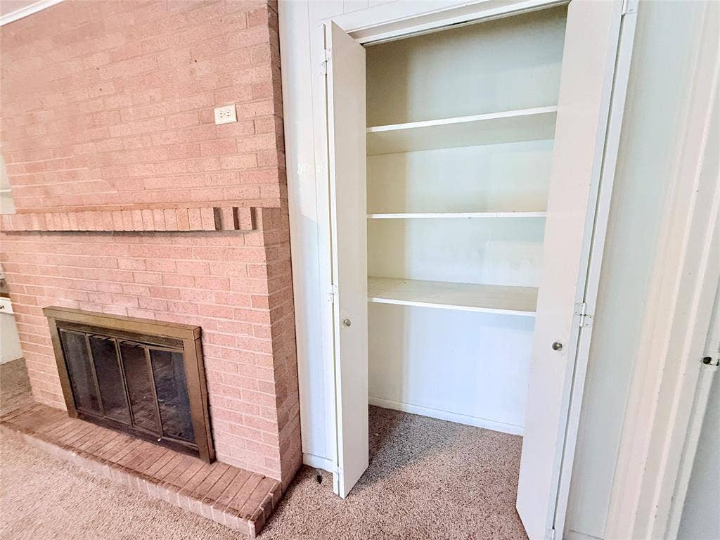 1500 S Houston, Denison, TX 75020 Floor-to-ceiling brick fireplace with a metal firebox and mantel, accompanied by a built-in storage closet featuring shelving and bifold doors