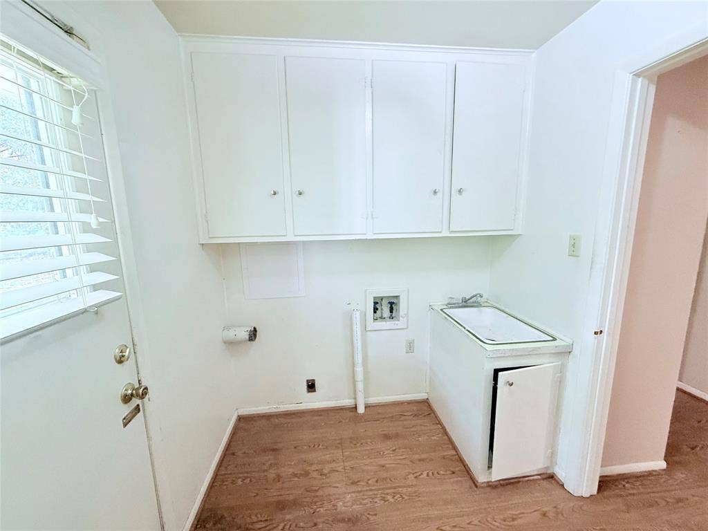 1500 S Houston, Denison, TX 75020 Utility room featuring wood-finish flooring, white wall-mounted cabinetry, a built-in basin sink with cabinet storage, and exterior door access