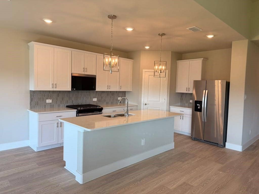 1313 Winters Way, Princeton, TX 75071 Kitchen featuring white shaker-style cabinetry, quartz countertops, a central island with a double-basin sink, geometric pendant lighting, and wood-finish flooring