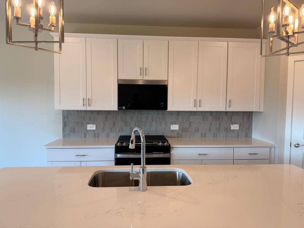1313 Winters Way, Princeton, TX 75071 Kitchen featuring white shaker-style cabinetry, quartz countertops, a patterned tile backsplash, stainless steel undermount sink with a gooseneck faucet, and two industrial-style pendant light fixtures