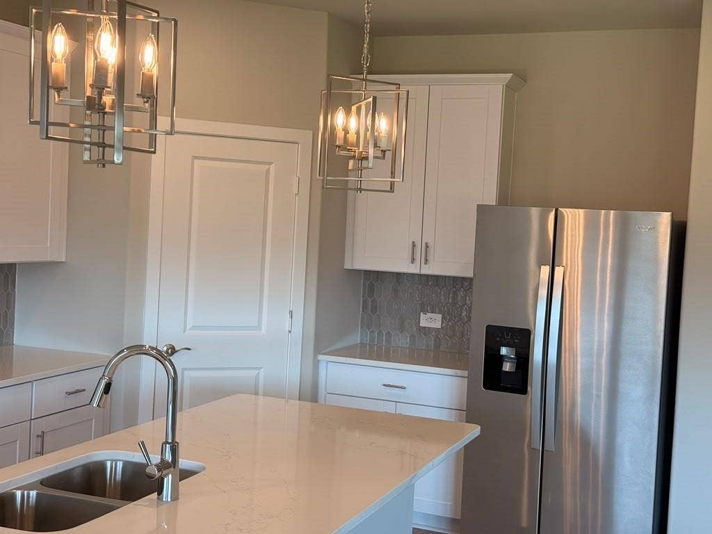1313 Winters Way, Princeton, TX 75071 Kitchen featuring white cabinetry, solid surface island countertop, stainless steel refrigerator, geometric pendant lighting, and a neutral-toned tile backsplash