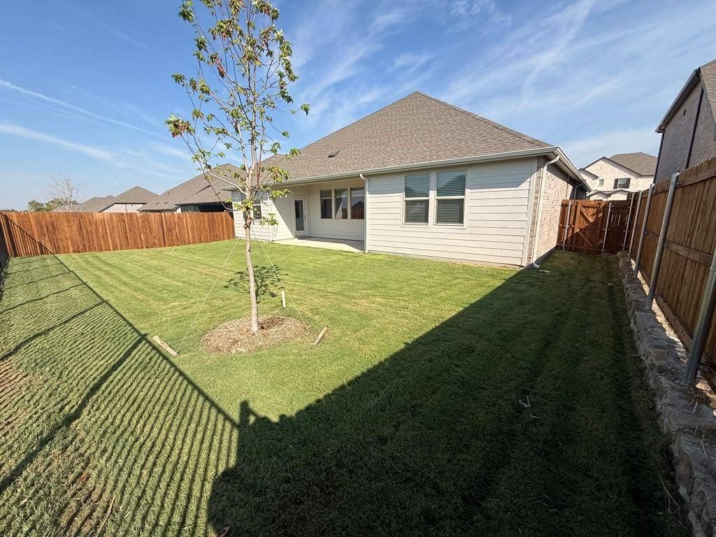 1313 Winters Way, Princeton, TX 75071 Private fenced backyard featuring a grass lawn, stone retaining wall, and horizontal wood-style fencing