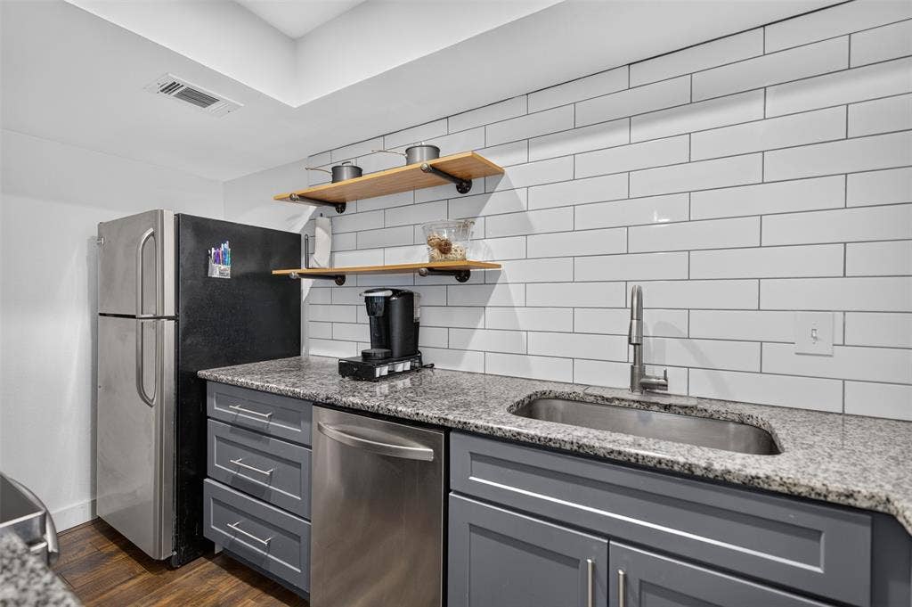 2851 Ursa Circle, Garland, TX 75044 Kitchen featuring stone-finish countertops, subway tile backsplash, shaker-style cabinetry, stainless steel dishwasher, and built-in wood shelving