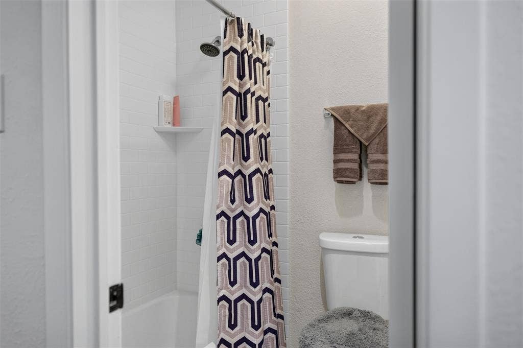 2851 Ursa Circle, Garland, TX 75044 Full bathroom featuring white subway tile shower surround, integrated corner shelf, wall-mounted towel bar, and standard-height toilet