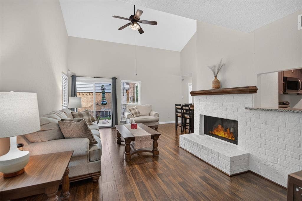 2851 Ursa Circle, Garland, TX 75044 Vaulted ceilings, wood-finish flooring, white painted brick fireplace with a wood mantel, ceiling fan, and sliding glass door leading to an outdoor space