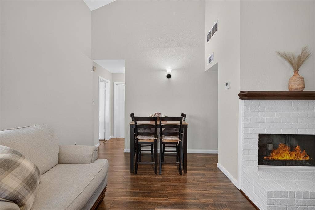 2851 Ursa Circle, Garland, TX 75044 Living area featuring double-height ceilings, wood-finish flooring, and a white brick fireplace with a wood mantel