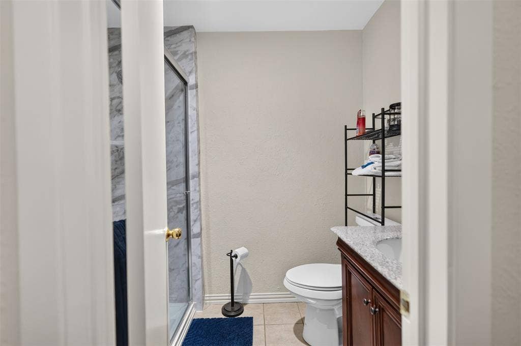 2851 Ursa Circle, Garland, TX 75044 Bathroom featuring a shower stall with stone-finish surround, wood-tone vanity, stone-finish countertop, and tile flooring