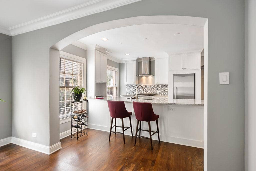 Kitchen featuring an arched entryway, white cabinetry, stone-finish countertops, stainless steel appliances, and wood-finish flooring