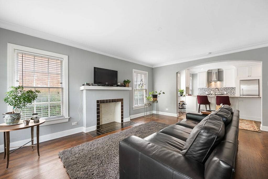 Living area featuring wood-finish flooring, a fireplace with a decorative tile surround and mantel, multi-pane windows, and an arched entryway