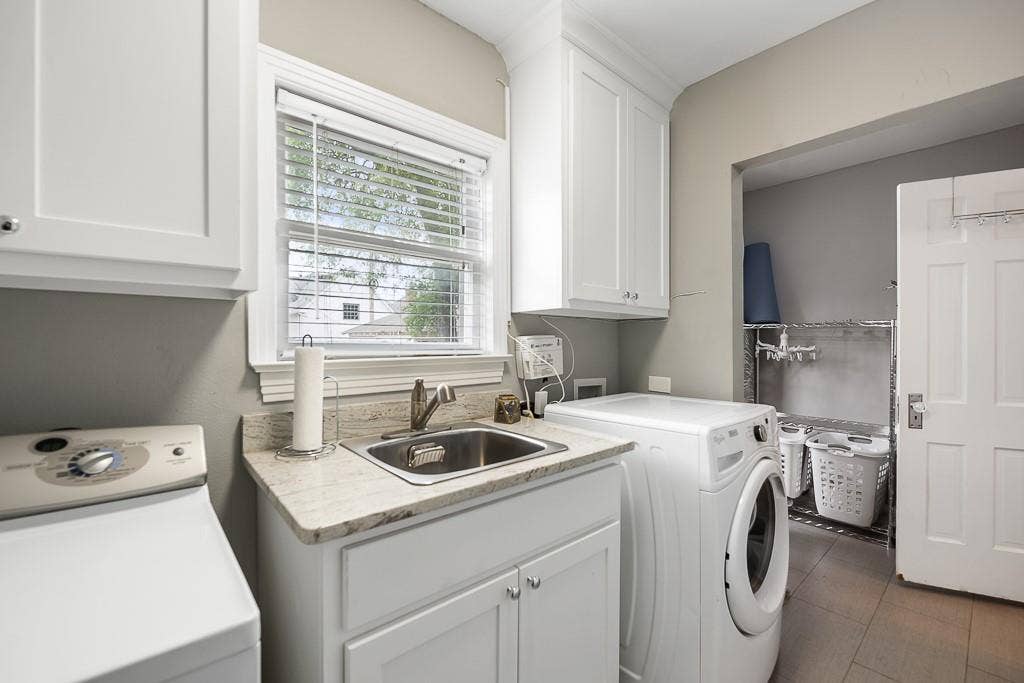 Laundry room featuring white cabinetry, stone-finish countertops, an undermount stainless steel sink with a pull-down faucet, and neutral tile flooring