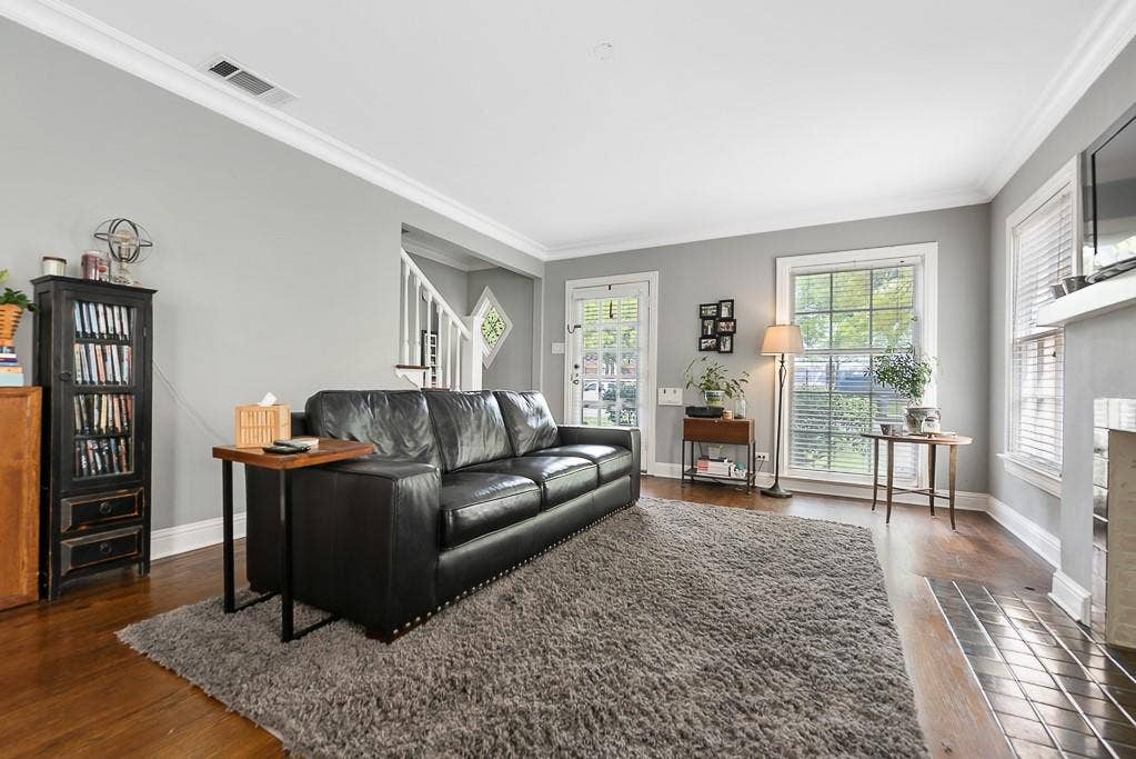 Living room featuring wood-finish flooring, crown molding, double-hung windows with integrated blinds, and a tiled fireplace surround