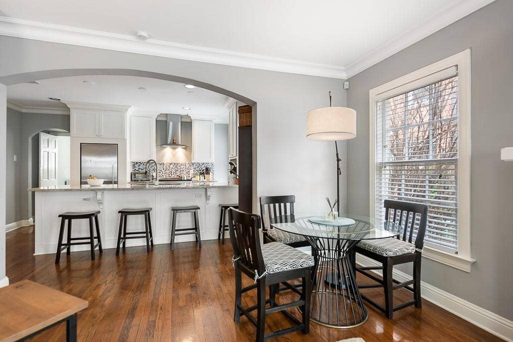 Kitchen featuring white cabinetry, stone-finish countertops, stainless steel appliances, and a tiled backsplash, accented by wood-finish flooring and an arched architectural opening