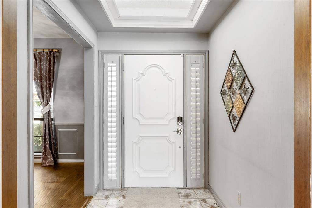 2510 Buttercup Drive, Richardson, TX 75082 Welcoming entry foyer featuring a beautifully detailed front door flanked by plantation shutters and enhanced by a skylight for natural light. Crisp white trim and neutral finishes create a bright, polished first impression with a seamless view into the formal dining area.