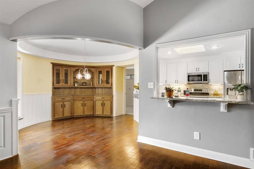 2510 Buttercup Drive, Richardson, TX 75082 Charming breakfast nook featuring a curved architectural design, rich wood flooring, classic wainscoting, and a beautiful built-in wood hutch with glass-front cabinetry. Elegant pendant lighting and abundant natural light create a warm, inviting space for casual dining and morning gatherings.