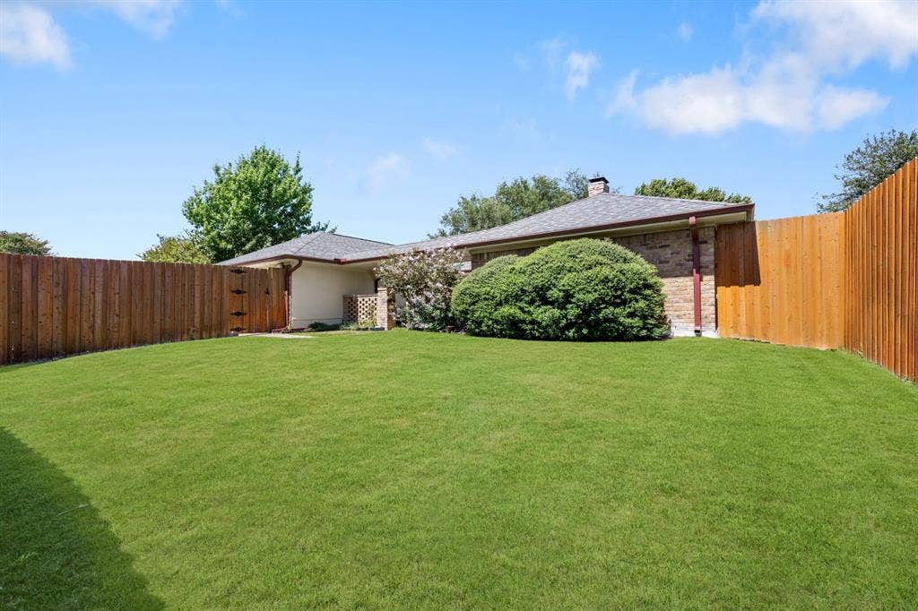 2510 Buttercup Drive, Richardson, TX 75082 Beautifully landscaped backyard offering an expansive, lush lawn framed by mature greenery and a privacy-enhancing wood fence. A covered patio provides a comfortable outdoor retreat, creating a wonderful setting for relaxing, entertaining, and enjoying the outdoors. *Grass enhanced to show potential*