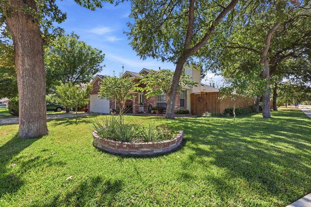 873 Hope Lane, Irving, TX 75061 Brick exterior residence featuring a circular masonry planter bed, mature trees, and a wooden privacy fence