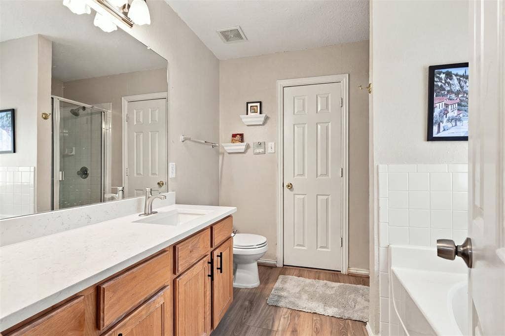 873 Hope Lane, Irving, TX 75061 Bathroom featuring a vanity with a light-toned countertop, wood-finish cabinetry with matte black hardware, a full-width wall mirror, and a glass-enclosed shower