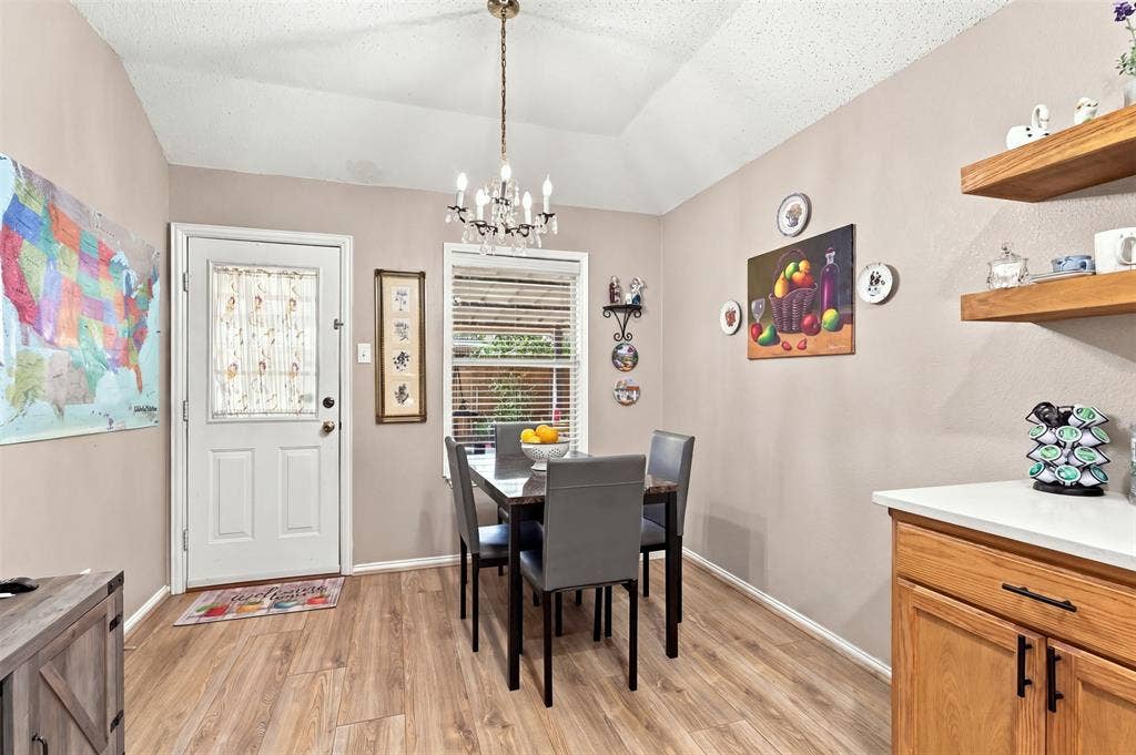 873 Hope Lane, Irving, TX 75061 Vaulted ceiling with an overhead chandelier, wood-finish flooring, built-in wooden shelving, and a solid-core entry door with an integrated glass panel