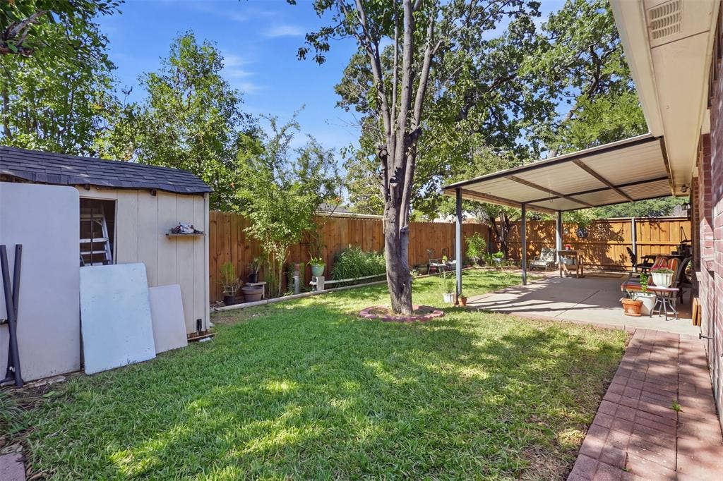 873 Hope Lane, Irving, TX 75061 Backyard featuring a concrete covered patio, brick-paved walkway, detached storage structure, and perimeter wood fencing