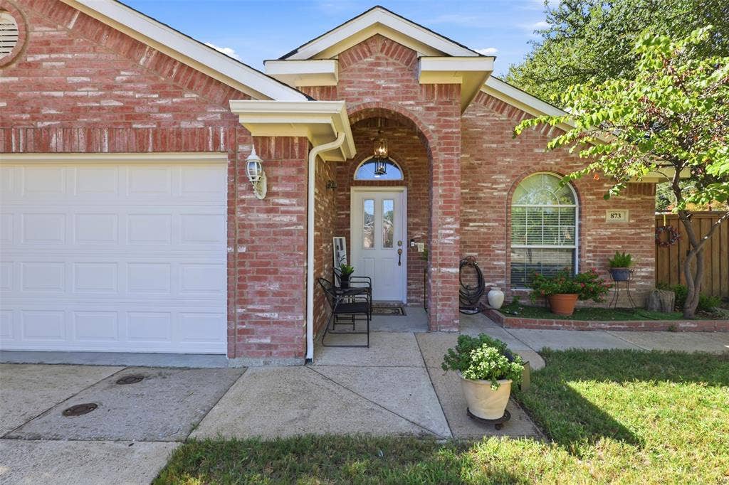 873 Hope Lane, Irving, TX 75061 Brick exterior featuring a gabled roofline, arched entryway, white paneled front door with a transom window, and an attached two-car garage