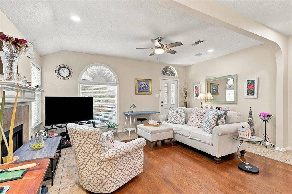 873 Hope Lane, Irving, TX 75061 Vaulted ceiling with a centrally mounted ceiling fan, arched windows, stone-surround fireplace, and wood-finish flooring